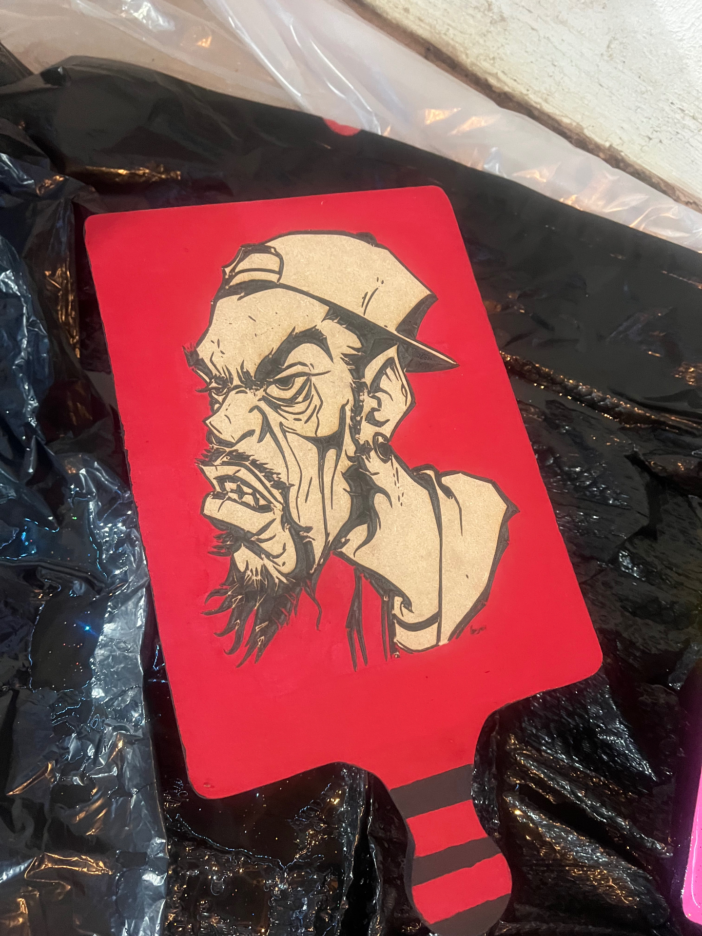 Red painted wooden paddle with a laser-engraved portrait of a man in a backwards cap