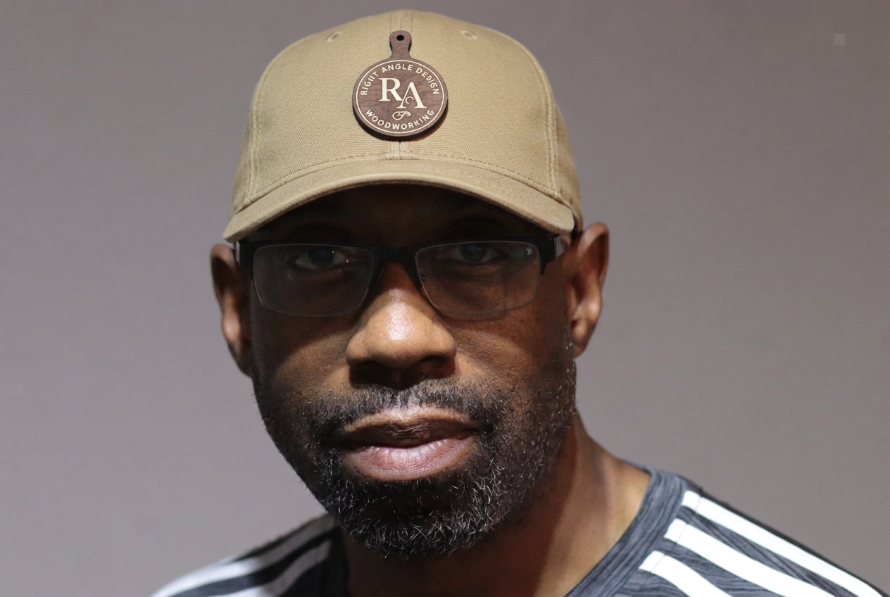 Virgil wearing a tan canvas baseball cap with a walnut cutting-board patch carrying the RA logo
