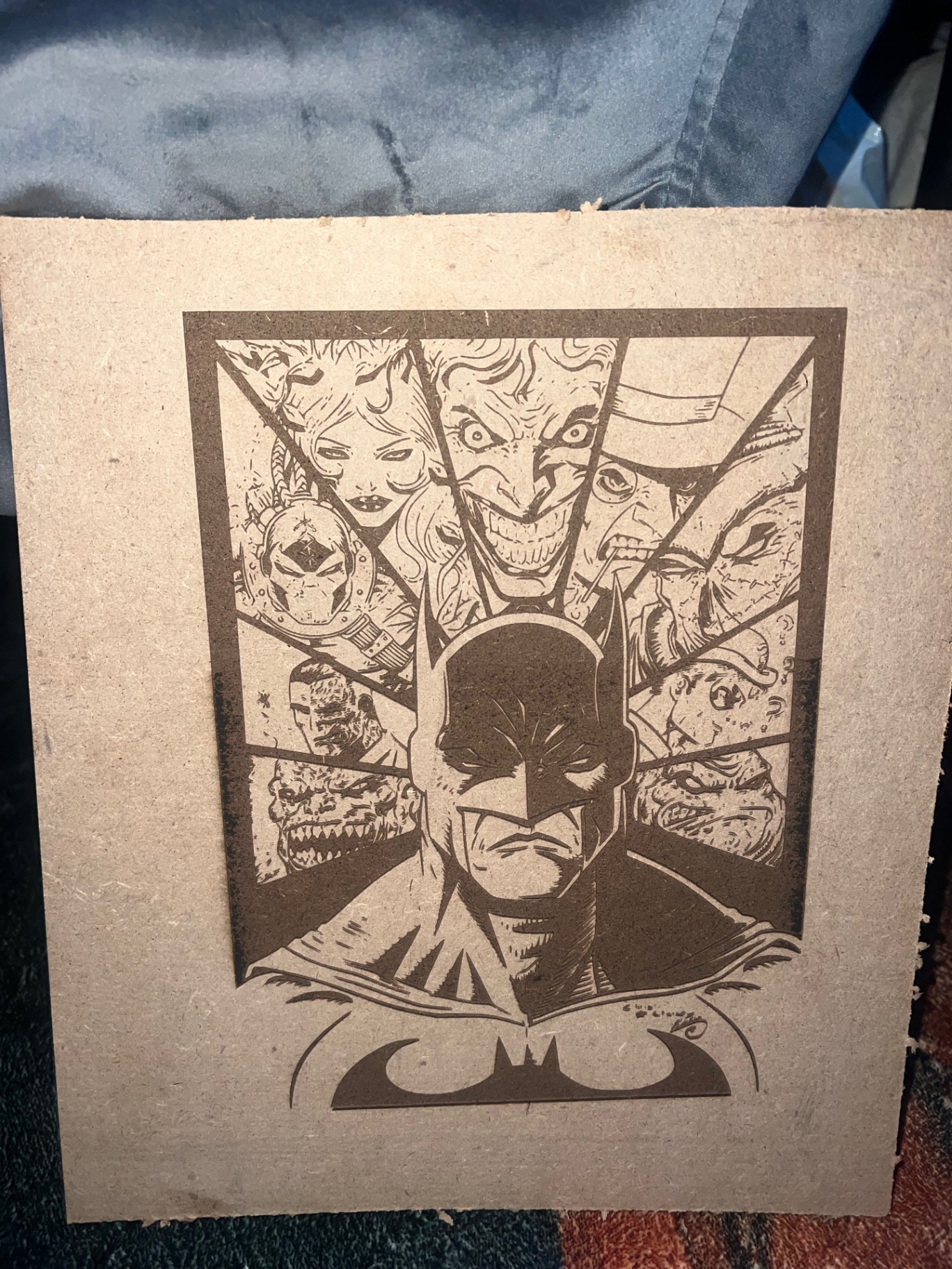 Laser-engraved panel of a caped hero surrounded by his rogues gallery, burned into natural board